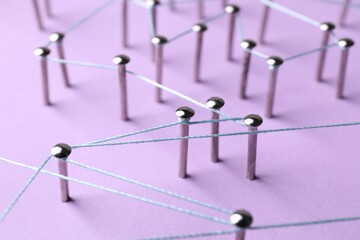 Network connection. Nails linked together by thread on violet background, closeup