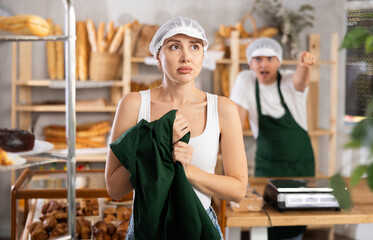Upset young girl standing with her back to angry salesman pointing at the door in bakeshop
