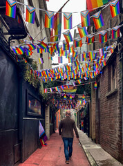 Ein Mann (von hinten) geht durch eine schmale Gasse mit vielen Progress Pride Flag in Cork, Irland