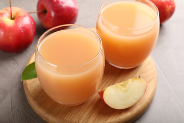 Tasty apple juice in glasses and fresh fruits on grey table, closeup