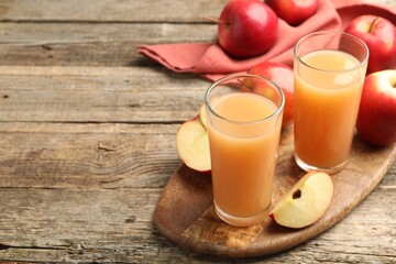 Tasty apple juice in glasses and fresh fruits on wooden table, space for text