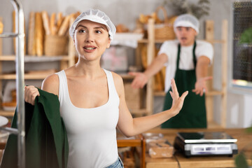 Content young girl leaving her workplace in bakery while salesman behind her is looking frustrated