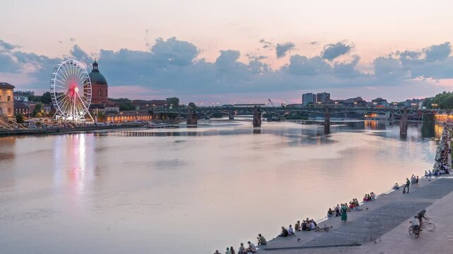 Aerial view of Port de la Daurade park along the Garonne River day to night transition timelapse in Toulouse, France. La Grave Hospital with Saint-Pierre Bridge after sunset with colorful clouds