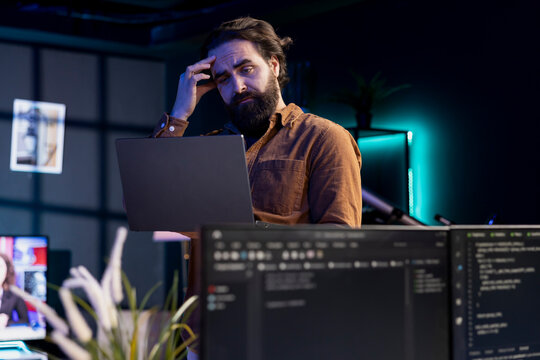 Programmer scratching head in confusion trying to secure company servers from virus attacks. Hesitant IT remote employee unsure how to fix code, trying to building firewalls protecting data