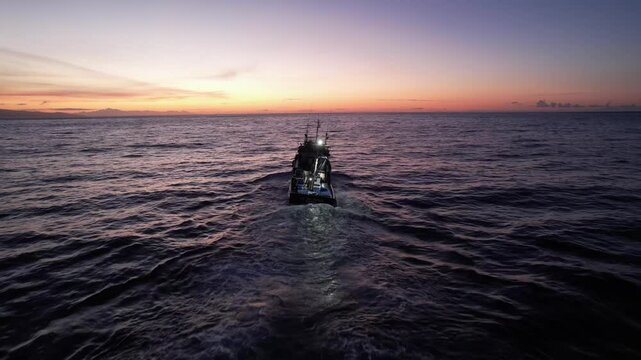 Imagem de um atuneiro navegando tranquilamente nas &aacute;guas do Oceano Atl&acirc;ntico, com o sol nascente iluminando o horizonte.