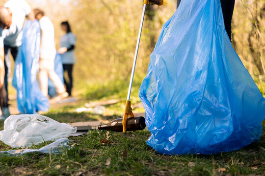 Volunteers group gathering to tidy up the woods of garbage, fighting forest pollution to protect the natural ecosystem. Team of activists collecting rubbish and plastic waste with tools.