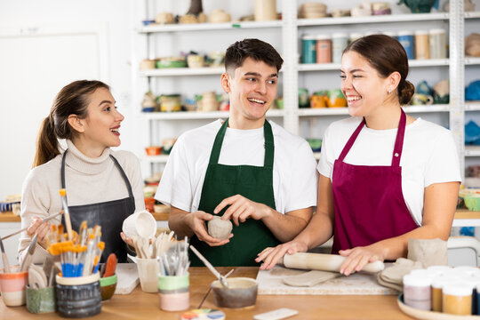 Two young women and young man making clay pottery in workshop