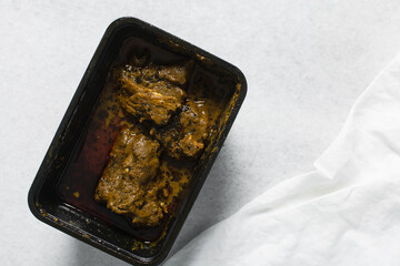 Overhead view of Nigerian banga soup with fish and beef in a plastic container, top view of palm nut soup in a takeaway plate, traditional palm nut soup in a black plate