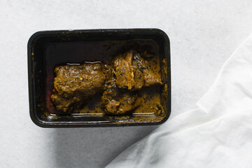 Overhead view of Nigerian banga soup with fish and beef in a plastic container, top view of palm nut soup in a takeaway plate, traditional palm nut soup in a black plate