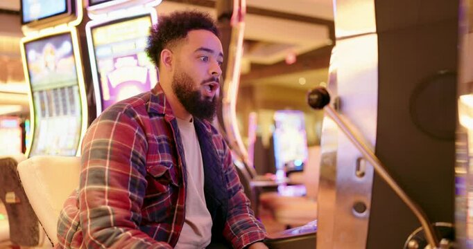 A focused young man engrossed in the excitement of a slot machine at a vibrant and bustling casino, fully embodying the thrill of the game and nurturing a strong hope for a significant win