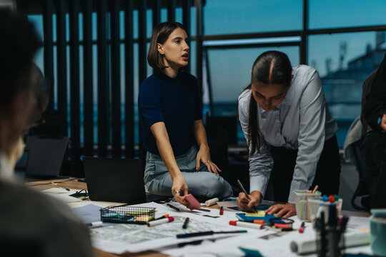A diverse team of business people collaborating and discussing ideas late at night to meet deadlines. The busy meeting atmosphere highlights teamwork, creativity, and strategic problem-solving. - Powered by Adobe