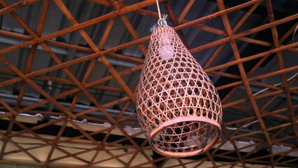 A stunning, woven bamboo pendant lamp hangs gracefully from a wooden ceiling, creating a warm,...