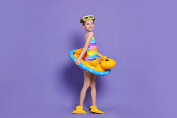 Happy girl in beachwear with diving mask, flippers and inflatable ring on purple background © New Africa