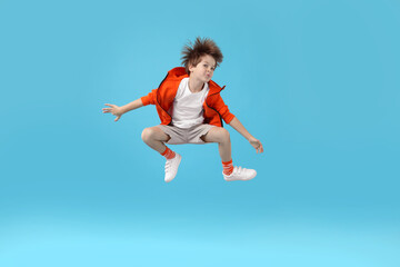 Happy little boy jumping on light blue background