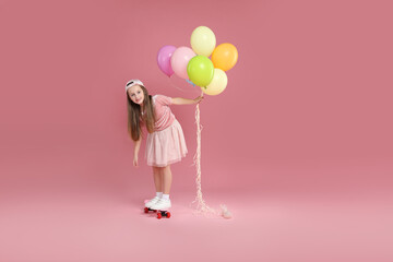 Little girl with colorful balloons standing on penny board against pink background