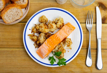Cooked salmon fillet with cauliflower and parsley on a plate on a wooden table. Nutritious diet lunch with fish and vegetables