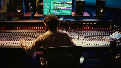 Sound designer mixing and mastering tracks on audio console in control room, using daw software on...