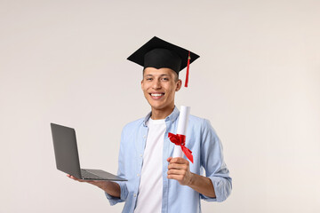 Happy student with laptop after graduation on light grey background
