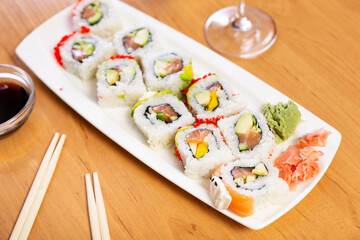 Sushi roll with red tobiko caviar on white plate on bamboo wooden table. Japanese menu concept