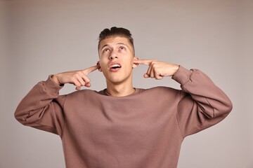 Annoyed young man covering his ears due to loud sound on light grey background