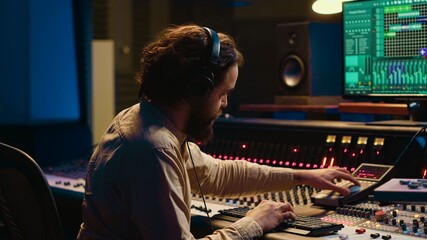 Audio expert operating motorized faders and mixing console in control room, using sliders and...