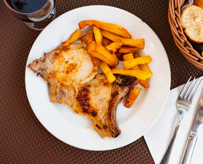 Hearty dish of European cuisine - juicy fried pork chops with ribs, supplemented with slices of French fries. Hearty dish for lunc. Whole meat grilled on barbecue garnished with potatoes