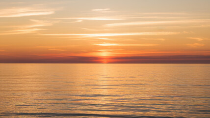 Naklejka premium A stunning sunset over calm waters, featuring vibrant orange and yellow hues against a clear sky, creating a serene and tranquil atmosphere.