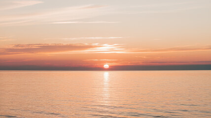 Naklejka premium A serene sunset over calm waters, casting a warm orange glow on the horizon, creating a peaceful atmosphere.