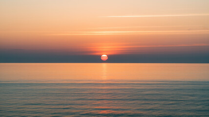 Naklejka premium A stunning sunset over the tranquil ocean, with vibrant hues of orange and pink reflecting on the water's surface.