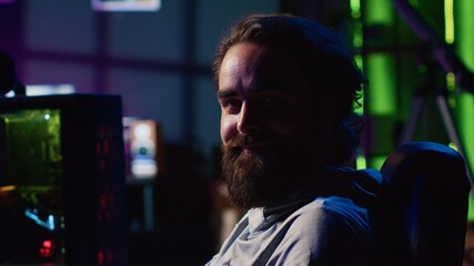 Man in dark living room playing video games on gaming PC at computer desk during leisure time. Gamer battling enemies in online multiplayer shooter from neon lights ornate home