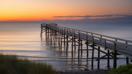 A tranquil wooden pier extends into the calm waters at sunset, casting reflections under a vibrant sky with hues of orange and purple.