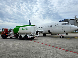 A tanker truck loaded with bio fuel, a sustainable aviation fuel is refueling a plane at the...