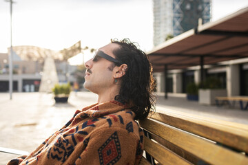 Relaxed man in sunglasses enjoying sunshine on urban bench