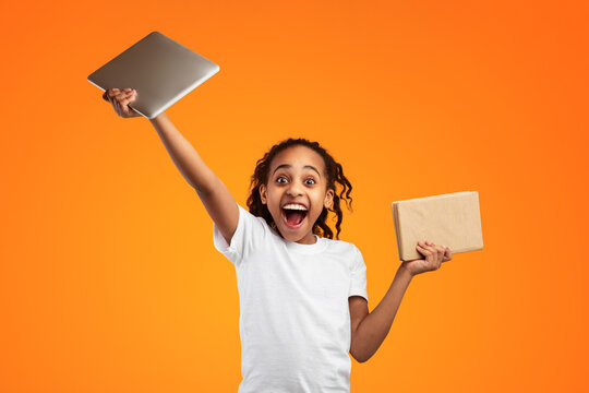 Books Vs Gadgets Concept. Portrait of excited African American girl holding digital tablet and paper manual, comparing them, raising hand with pc up. Modern Education, Youth And Learning