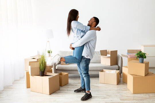 Loving african american couple celebrating moving day, guy lifting his wife in their new apartment, feeling happy moving into own house. Home relocation concept