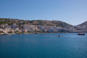 Fototapeta premium Resort town in Albania, view from a departing ship to houses and mountains. Port town of Saranda in Albania