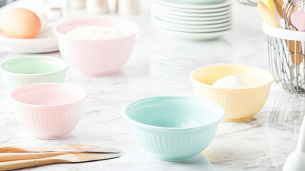 A marble countertop adorned with baking tools, including spatulas and measuring cups, surrounded by bowls filled with pastel-colored frosting, creating a cheerful baking atmosphere.