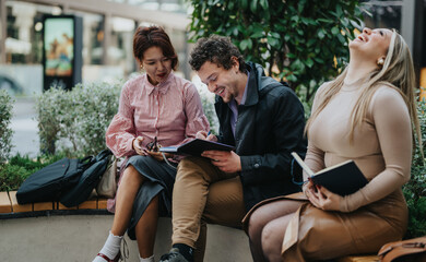 Three business people share a lighthearted moment while working outdoors on a break. They are...
