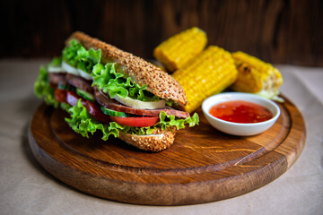 A fresh, vibrant sandwich with crisp vegetables and sesame bread, served alongside grilled corn and sauce — rustic, wholesome dining perfection.