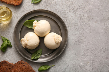 Plate of tasty Burrata cheese with basil and bread on grey table