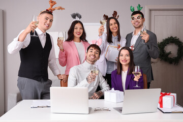 Happy young colleagues with champagne celebrating New Year at corporate party in office
