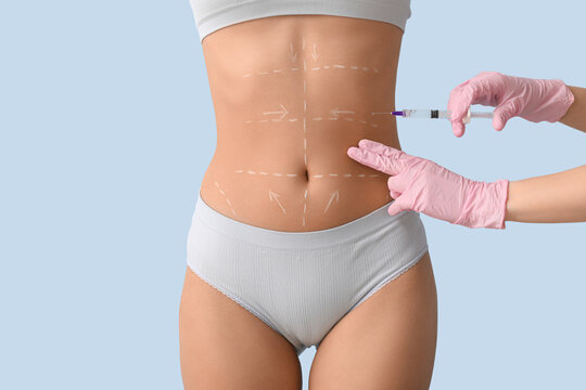 Plastic surgeon with injection and marks on woman's belly against light background, closeup