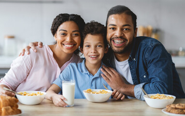 A joyful family shares a breakfast moment in their cheerful kitchen. Parents embrace their son as he smiles, surrounded by bowls of cereal, milk, and cookies, celebrating togetherness and love.