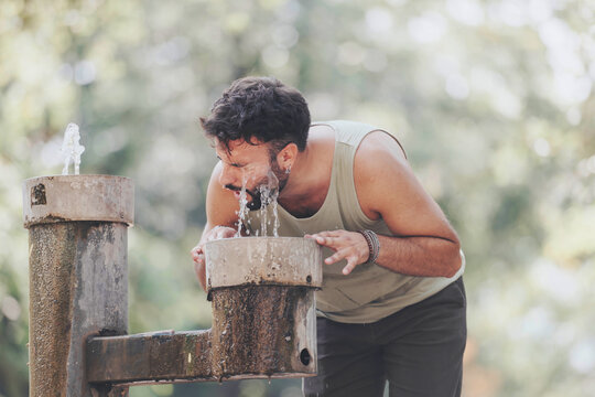 A man refreshes himself by drinking from a water fountain in a lush, sunlit park. This image captures hydration, outdoor leisure, and a connection with nature's calming beauty.