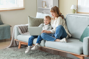 Happy mother and her little son with laptop sitting on sofa in living room at home