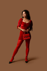 Beautiful young African-American woman in stylish red tights with handbag on brown background