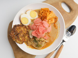Homemade rice cake or Lontong Sayur, cooked with vegetable curry and served with boiled egg, fritter, and crackers on white plate