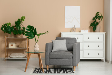 Modern interior of living room with tropical monstera leaves in vase on table and stylish armchair