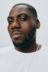 Obraz premium Portrait of a confident male model with a focused expression, wearing a simple white shirt, showcasing his sharp features against a neutral light gray background, emphasizing masculinity and self ass