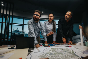 A diverse group of business professionals engaged in a strategic discussion over design plans. The team collaborates in a well-lit, modern office environment, focusing on innovation and problem